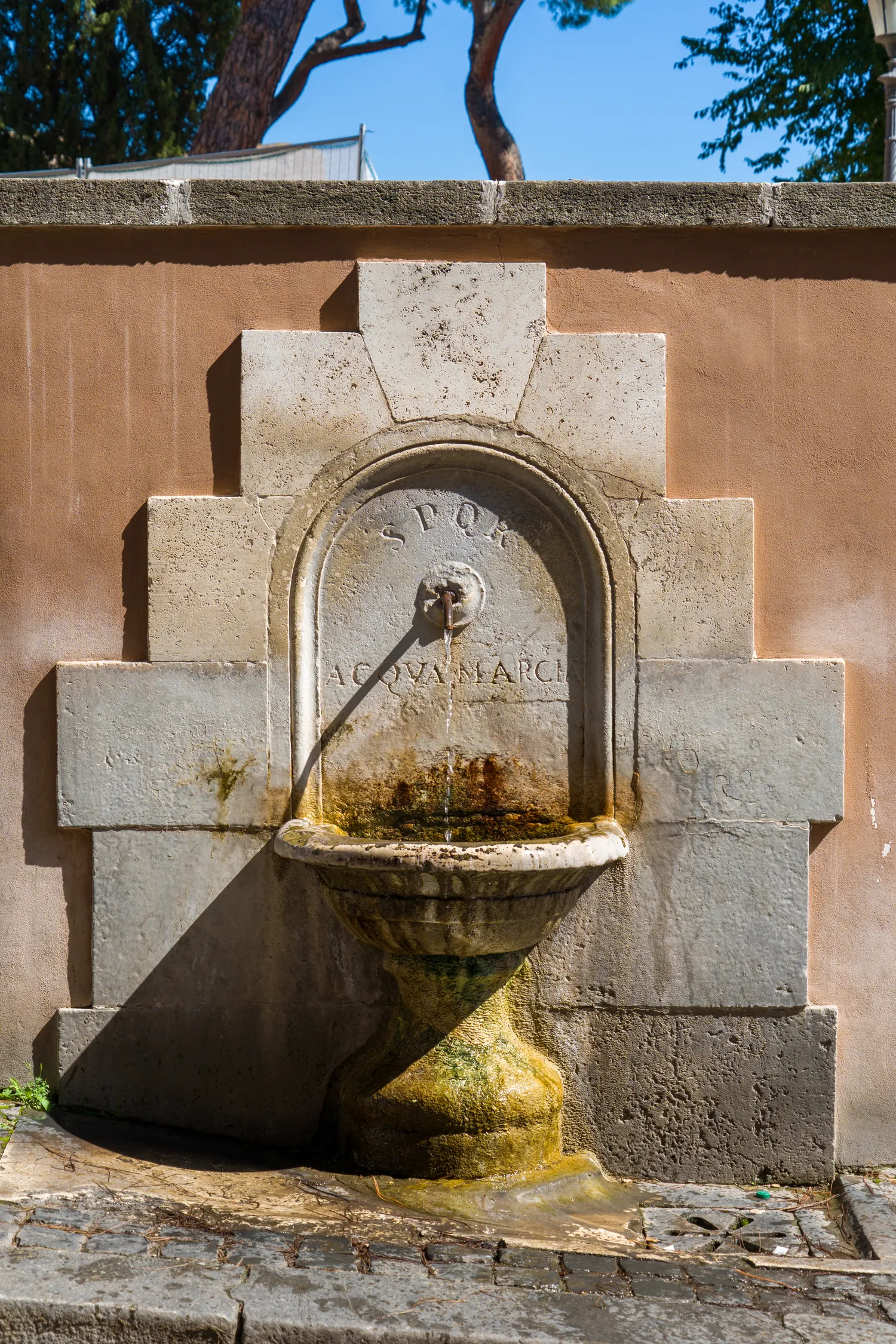 Fontanella in pietra con catino e acqua nella parete di una strada di Roma