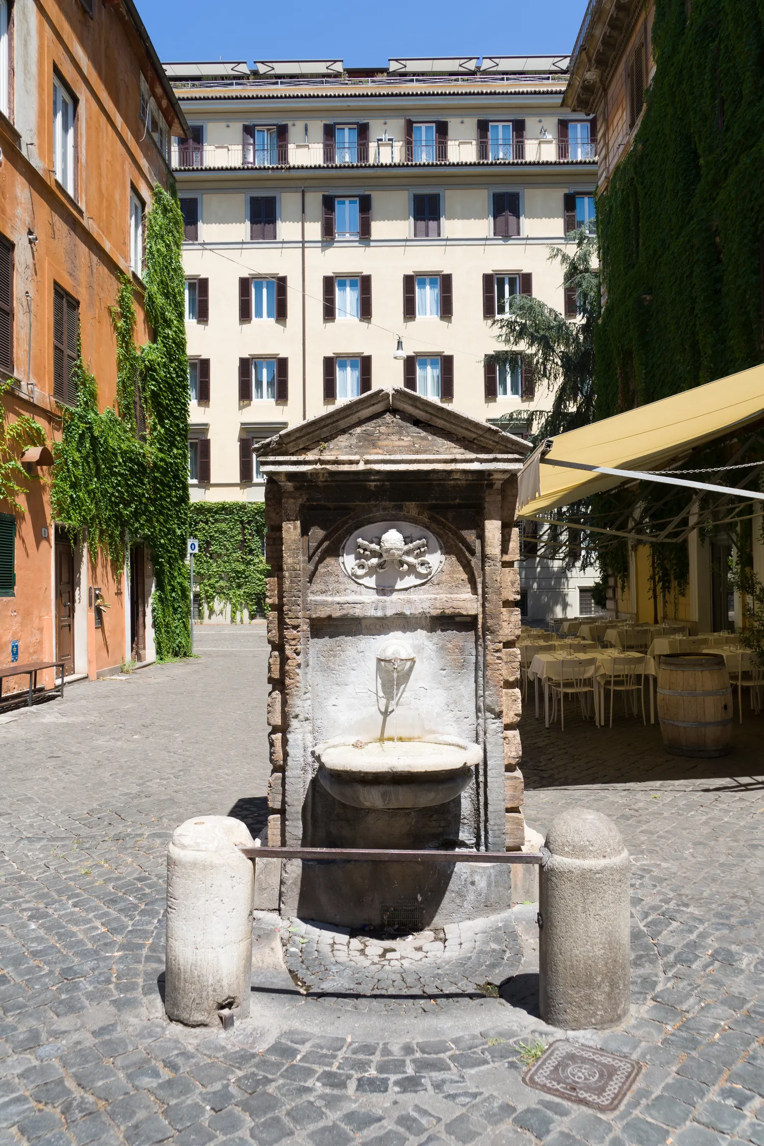 Fontanella rionale in pietra su una piazzetta romana con facciate ed edera