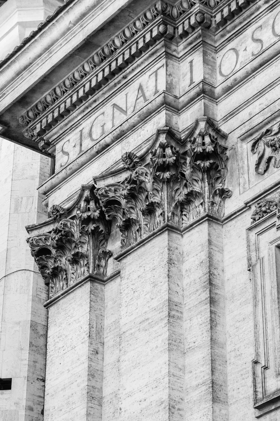 Iscrizione latina e capitelli di un edificio storico romano in bianco e nero