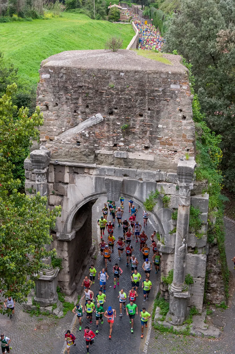 Runner che attraversano un arco antico durante una gara a Roma